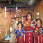an adult stands with a child on either side of them. They are all smiling, looking at the camera, and wearing brightly-colored traditional clothing