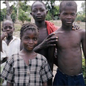 Four black boys—two of them shirtless and two in loose button-ups—pose for the camera. They all have serious expressions, except for the closest one, who stares at you with a knowing smirk