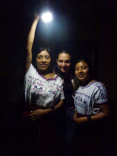 Three people stand in a pitch-black room, one of them holding a flashlight to illuminate the scene eerily from above