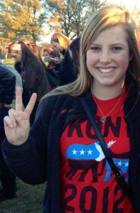 a woman in a red shirt and black fleece jacket holds up a peace sign one hand