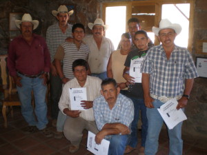 ten people, many in plaid shirts and cowboy hats, stand indoors with white paper certificates in their hands