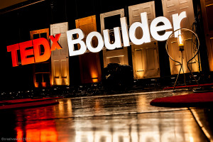 Huge 3D letters spelling "TEDx Boulder" hang in front of a window and reflect on the wet pavement.