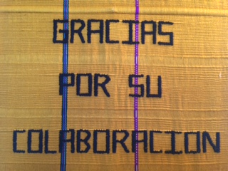 A hand-woven tapestry says "Gracias por su collaboration" in black thread