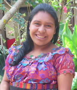 A headshot of Maria. She has an infectious smile, side-swept curled hair, light eyes, and a colorful embroidered blouse.