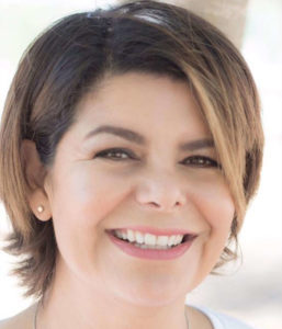 A headshot of Martha. She has a choppy, highlighted bob haircut, pink lipstick, and a big smile.