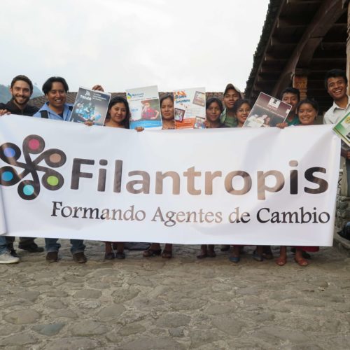 A dozen people hold up a large banner that says "Filantropis Formando Agentes de Cambio."