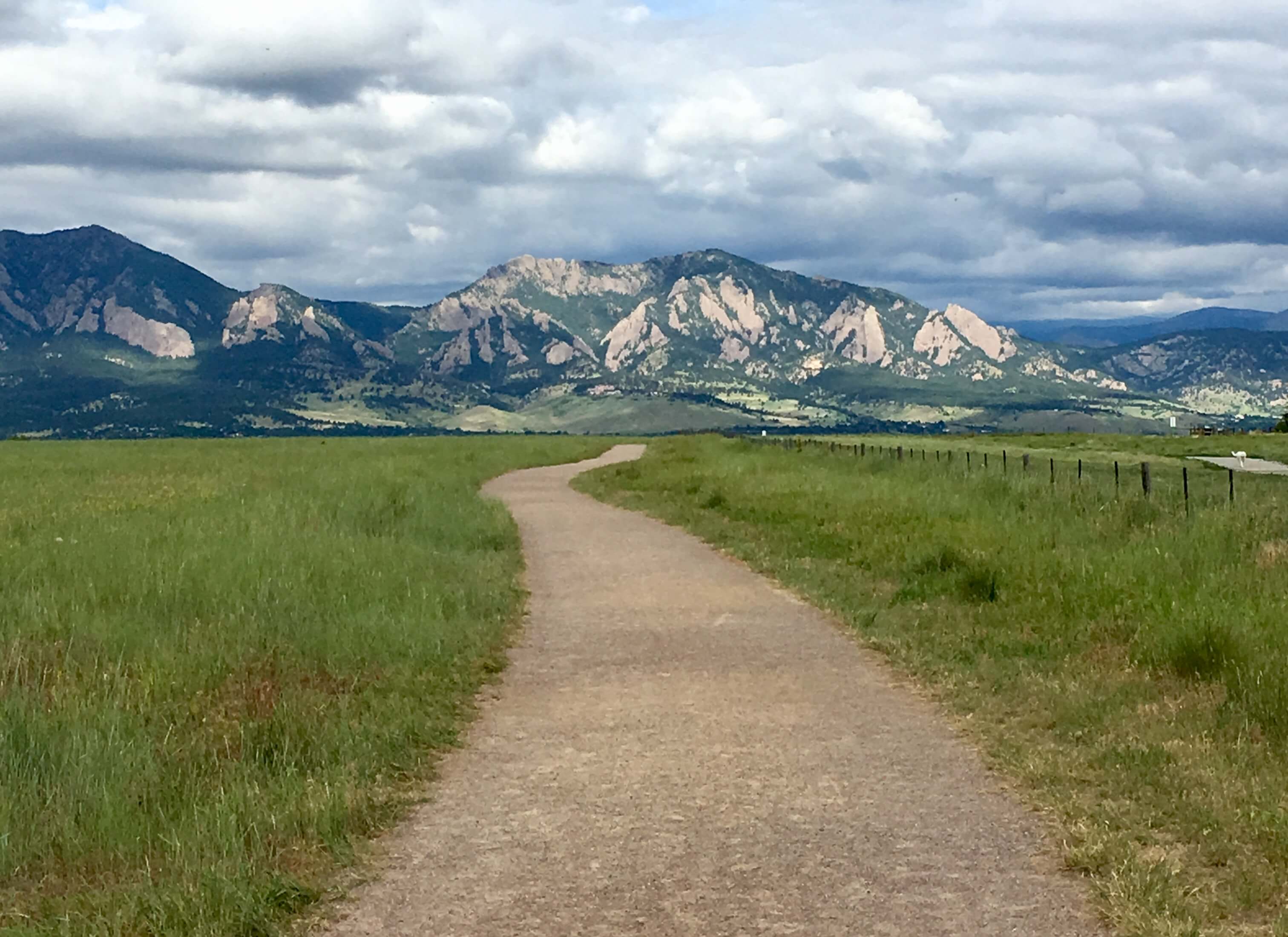 A dirt path lined with grass leads into the distance towards flatirons