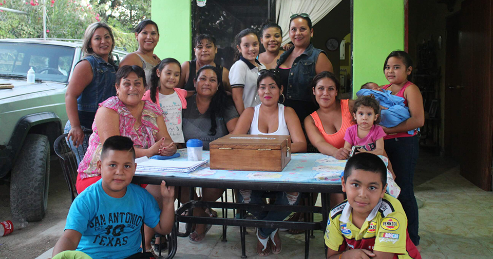 About a dozen people—mostly mothers and children— huddle around a small table with a wooden box on it.