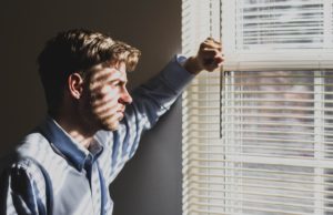 A white man with close-cropped hair and a baby blue button up looks thoughtfully out a window