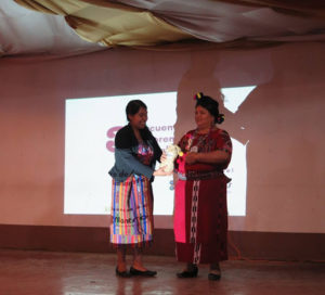 two people stand facing each other in front of a projected powerpoint. they are in the middle of a conversation or presentation.